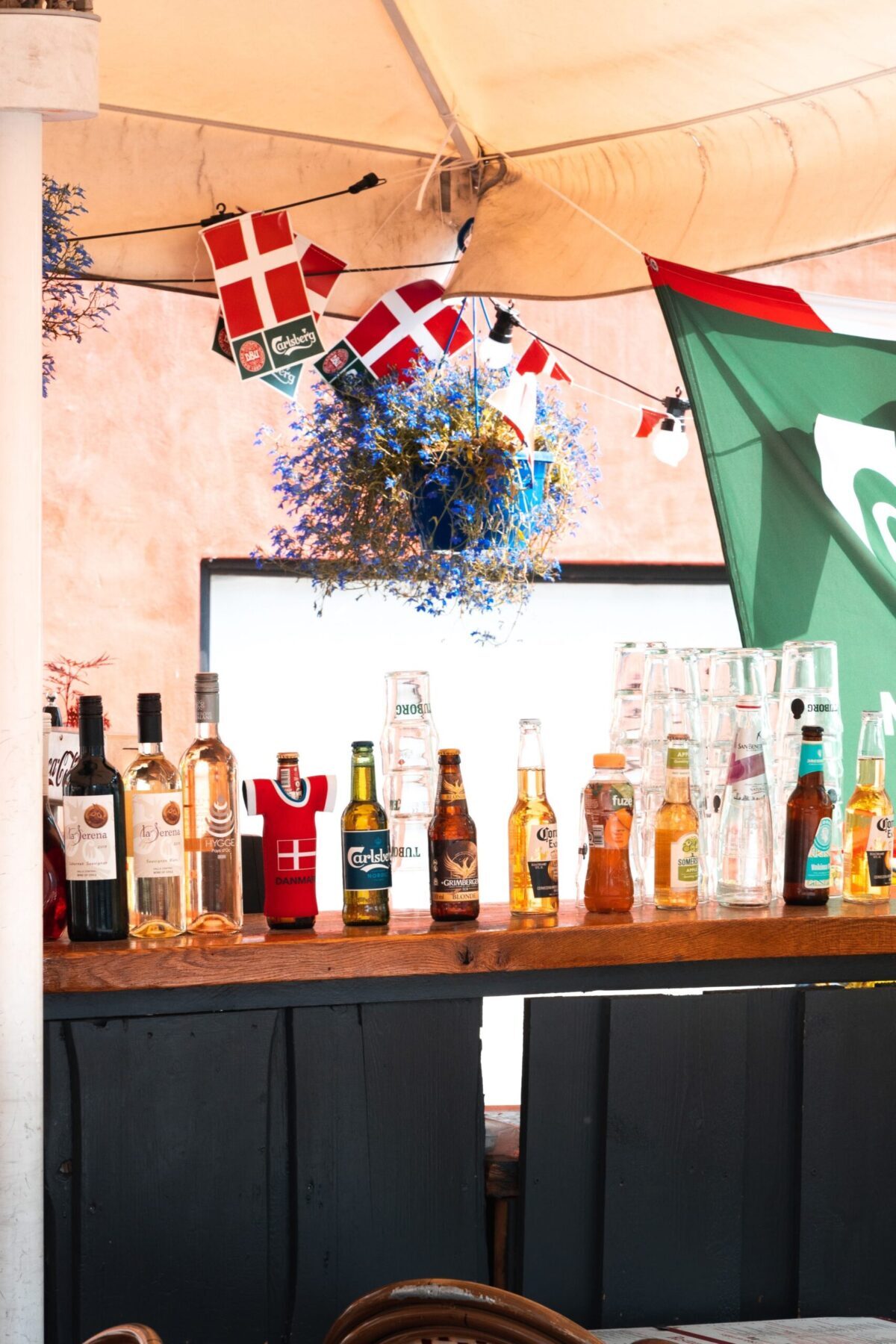 Bier hat Tradition in Dänemark. Verschiedene Flaschen auf einem Tresen, dahinter dänische Flaggen – Foto von Svend Nielsen auf Unsplash