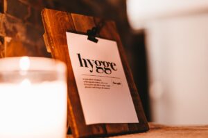 Das Wort Hygge auf einem Kalenderblatt, davor eine Kerze – Foto: Julian Hochgesang auf Unsplash