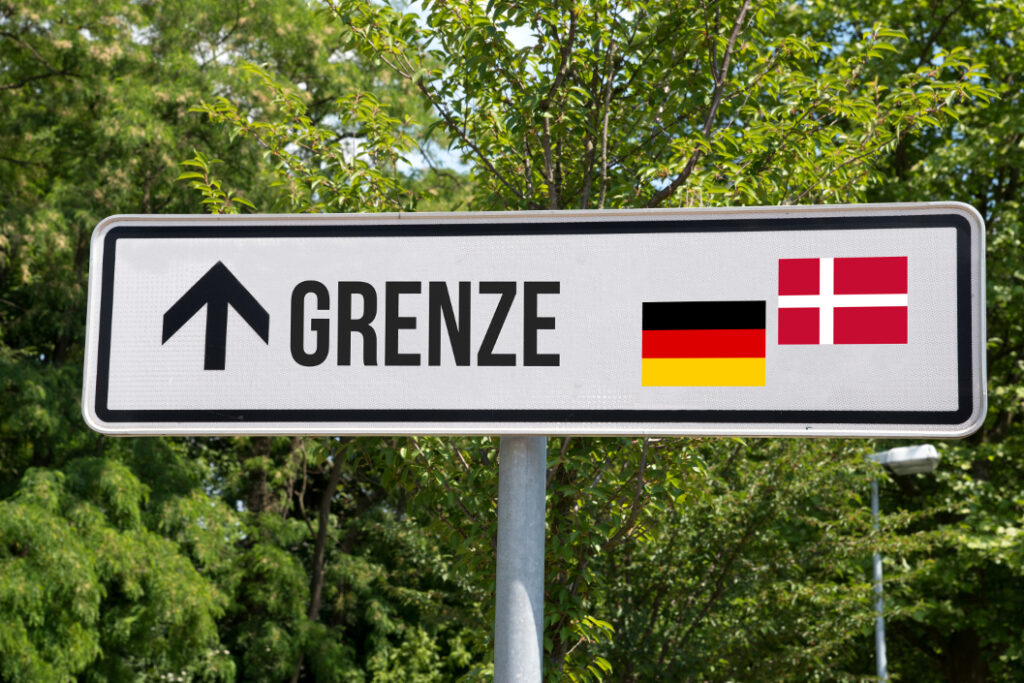 Bild von einem Hinweisschild mit Richtungspfeil und Flaggen an der deutsch-dänischen Grenze