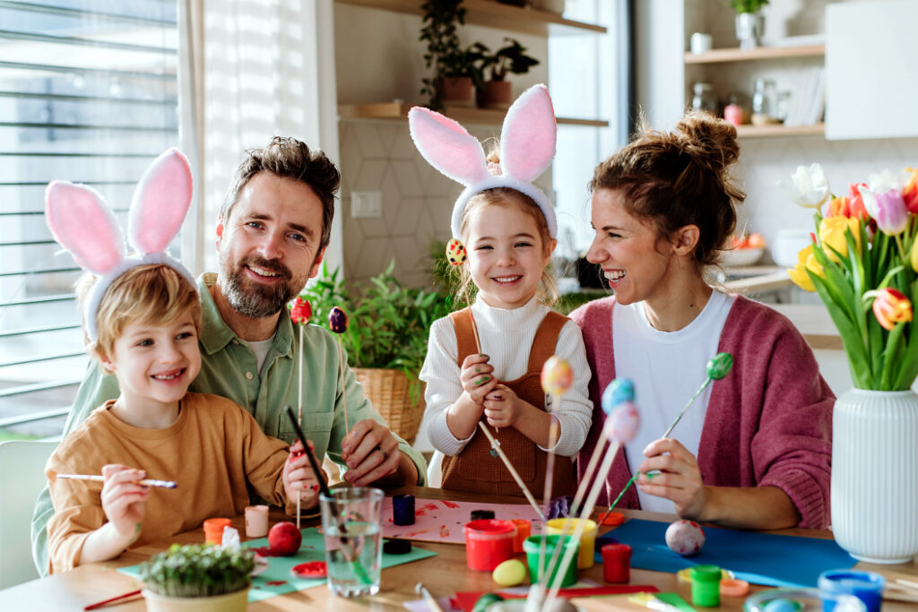 Familie mit zwei Kindern, die zu Ostern gemeinsam Ostereier in der Küche bemalen